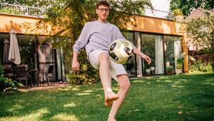 Junger Mann kickt einen Fussball barfüßig im Garten