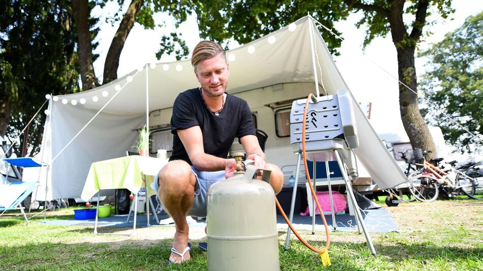 Mann schließt eine Gasflasche an einen Grill an
