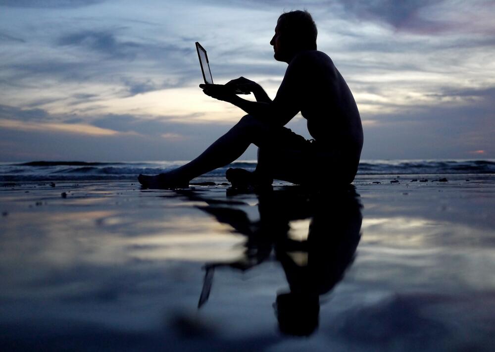 Mann arbeitet am Strand an einem Laptop