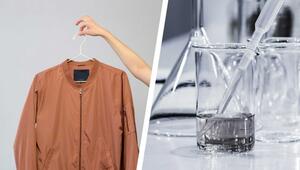 Links eine rostbraune Jacke an einem weißen Kleiderbügel, gehalten von einer Hand vor grauem ...