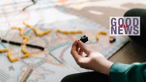Hand, die eine schwarze Spielfigur hält, im Vordergrund eines Spielbretts mit bunten ...