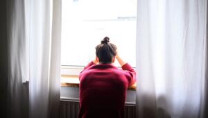 Eine Person an einem Fenster nimmt den Kopf in die Hände