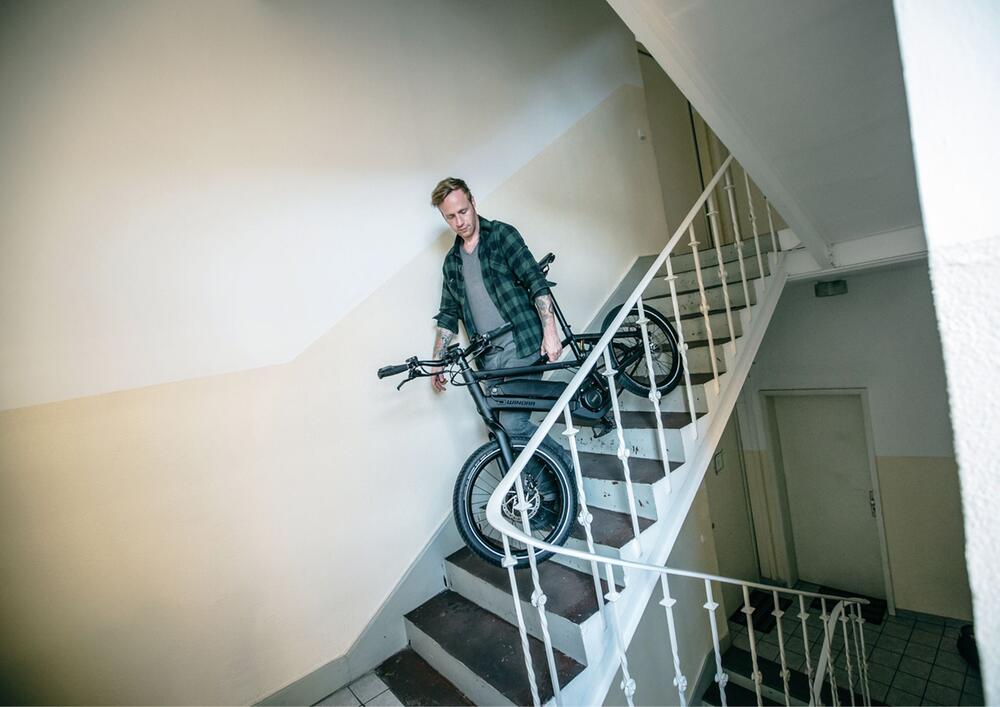 Ein Mann trägt E-Bike die Treppe in einem Mietshaus hinunter