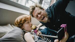 Vater singt ins Mikrofon, während das Kind im Bett liegt und das Mikro hält.