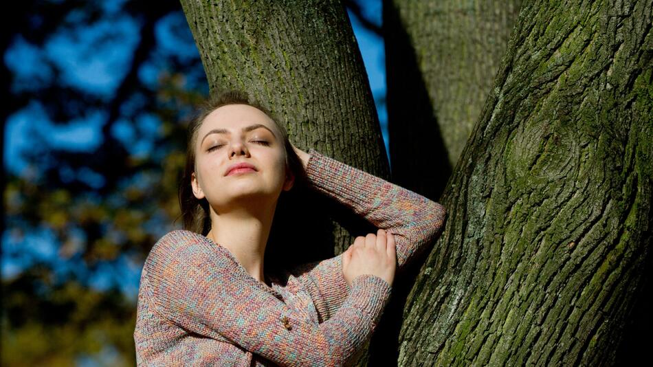 Frau lohnt mit geschlossenen Augen an einem Baum