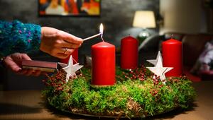 Eine Frau zündet eine Kerze auf einem Adventskranz an