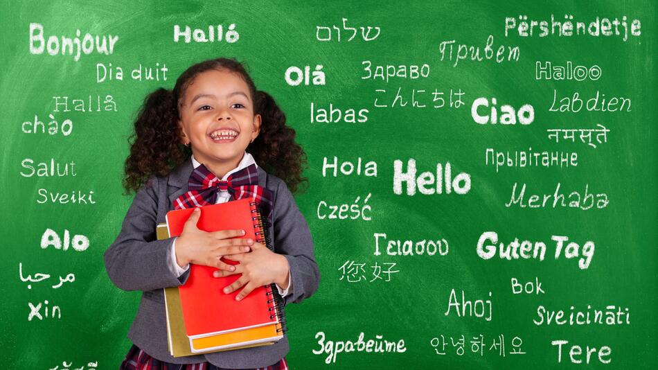 Mädchen steht vor einer Tafel, worauf "Hallo" in verschiedenen Sprachen steht.