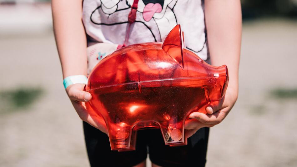 Ein Kind trägt ein rotes Sparschwein
