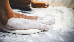 Eine Hand, die mit Mehl bedeckt ist, drückt einen flachen Teig auf einer bemehlten Arbeitsfläche.