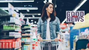 Frau mit Jeansjacke schiebt Einkaufswagen in einem Supermarkt, im Hintergrund Regale mit ...