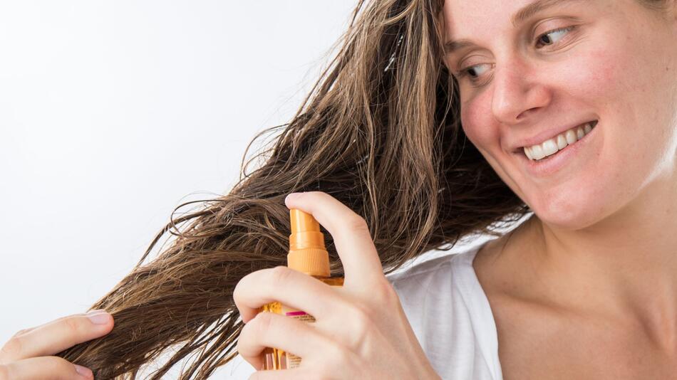 Frau sprüht Haare mit einem Pflegeprodukt ein