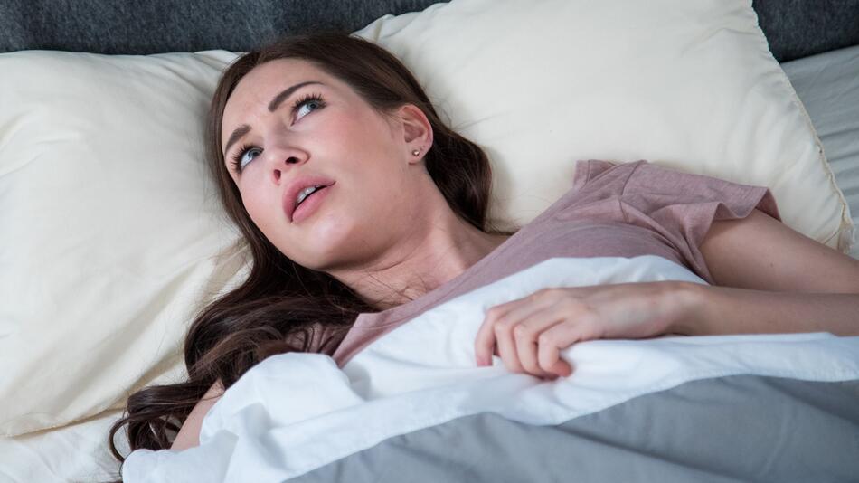 Eine junge Frau liegt wach in ihrem Bett