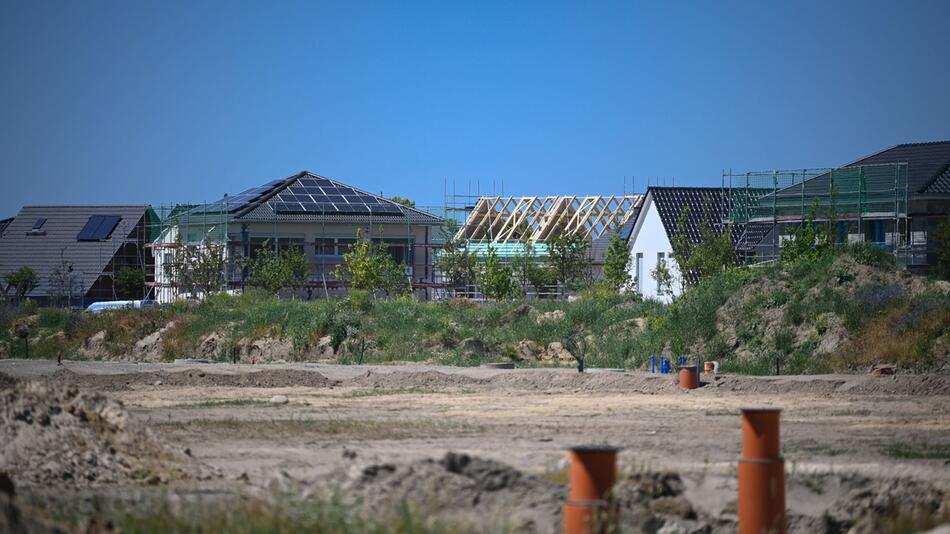 Einfamilienhäuser und Rohbauten stehen hinter einer Baustelle