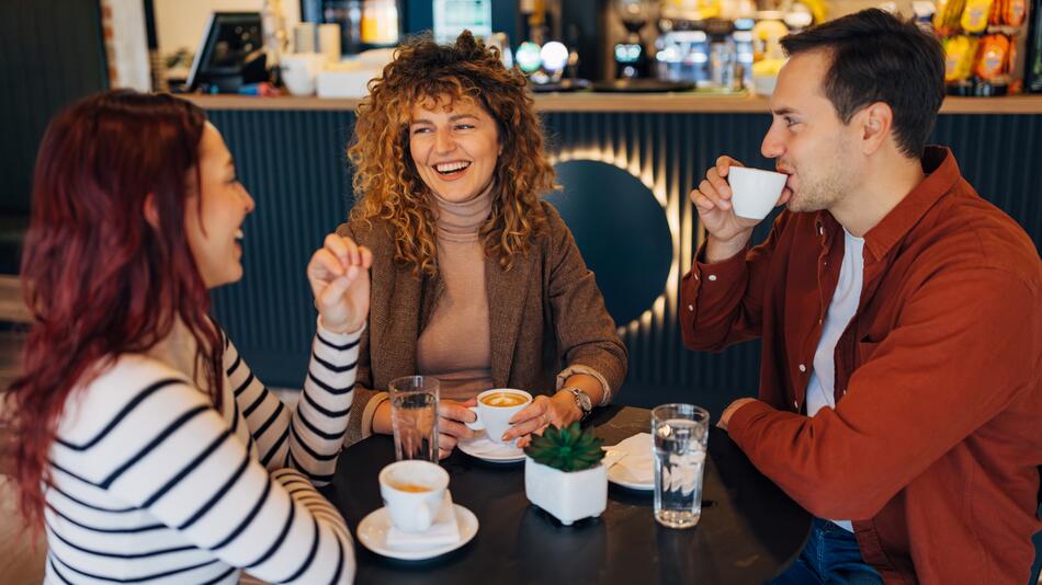 Drei Menschen in einem Café, lächeln sich gegenseitig an