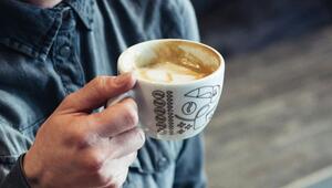 Hand, die eine weiße Tasse mit Kaffeeresten und Milchschaum hält, die Tasse ist mit schwarzen ...