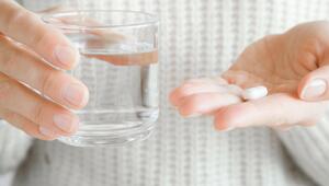 Frau hält ein Wasserglas, in der anderen Hand liegt eine Tablette