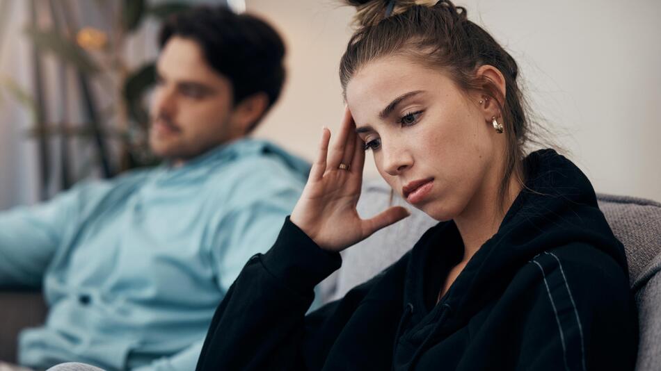 junge Frau sitzt genervt und traurig neben Freund auf dem Sofa