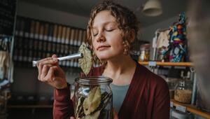 Eine Frau riecht an einem Lorbeerblatt. Sie hält ein Glas gefüllt mit Lorbeerblättern in der Hand.