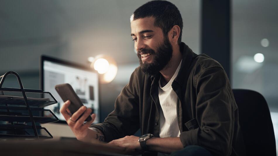 Mann sitzt am Tisch und schaut auf Handy