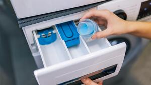 Frau gibt Waschmittel in ein offen stehendes Waschmittelfach 