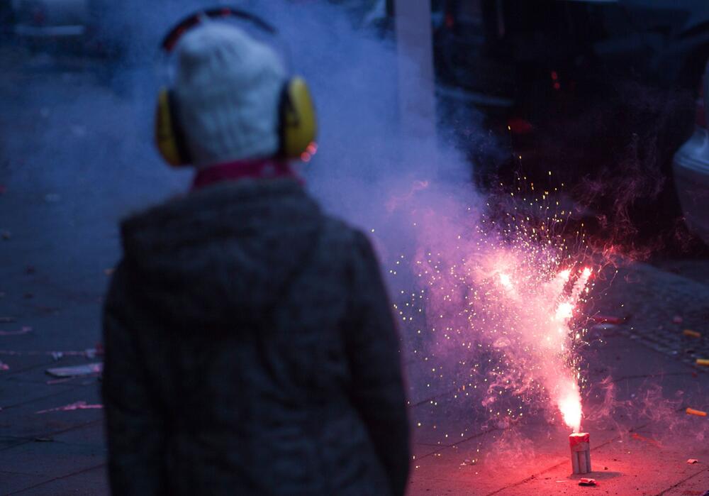 Kind mit Gehörschutz beobachtet Silvesterknaller