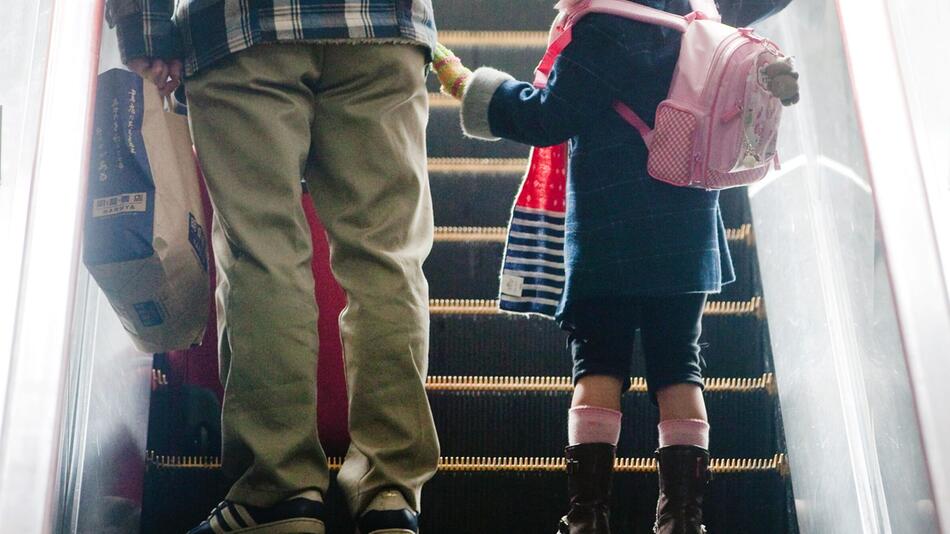 Mädchen steht neben ihrem Vater auf einer Rolltreppe