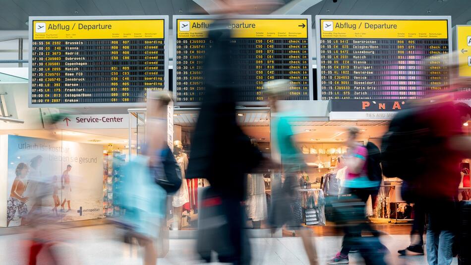 Passagiere laufen am Flughafen vor der Anzeigetafel