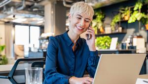 Eine Frau sitzt in einem Büro, lacht und telefoniert.