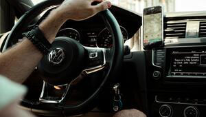 Mann hält ein Lenkrad eines Volkswagen-Autos, am Arm mehrere Armbänder, auf dem Armaturenbrett ...