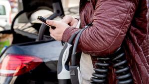 Ein Mann blickt an einer Ladesäule auf ein Smartphone