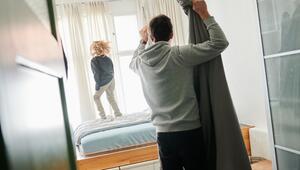 Ein Mann bezieht ein Bett während ein Kind auf dem Bett hüpft