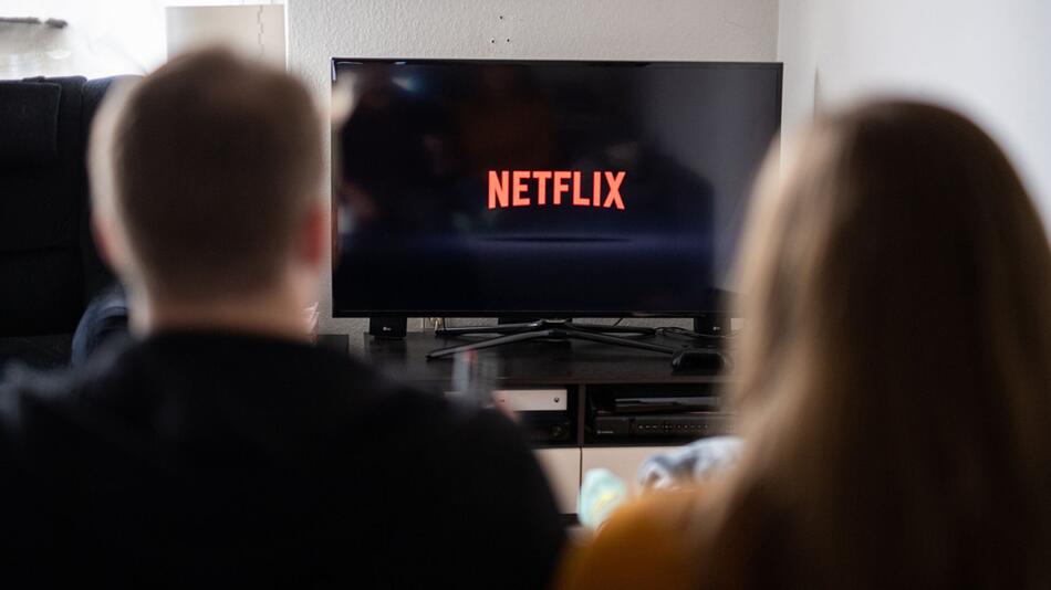 Paar sitzt vor Fernseher, auf dem das Netflix-Logo zu sehen ist