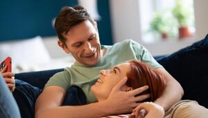 Eine Frau liegt auf dem Sofa auf dem Schoß ihres Mannes und lächelt ihn an.