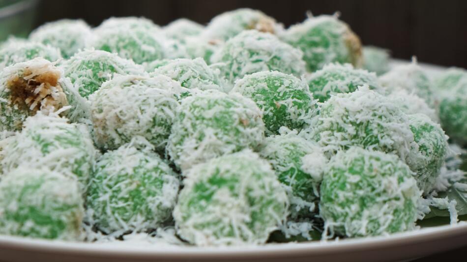 Indonesische Klepon werden mit Kokosraspeln bestreut und auf Bananenblättern serviert.