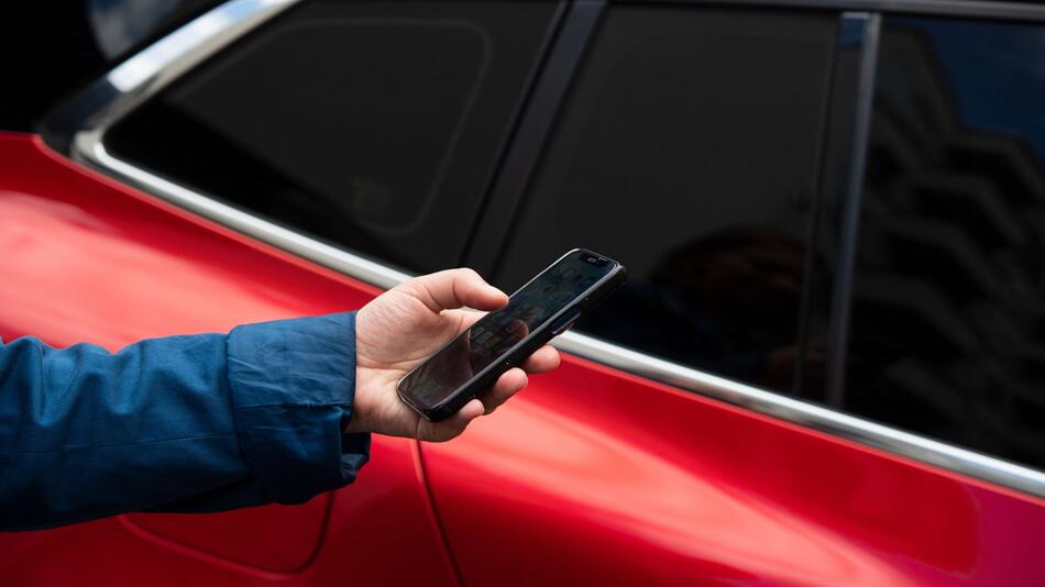 Eine Frau bedient ein Smartphone neben einem Auto