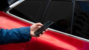 Eine Frau bedient ein Smartphone neben einem Auto