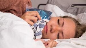 Eine Frau hält sich im Bett einen Kühlakku an die Wange