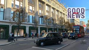 Straßenszene mit einem historischen Gebäude mit Säulen, mehreren Bäumen und Schaufenstern, davor ...
