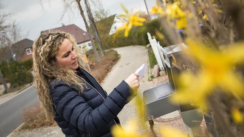 Eine Frau liest Post vor dem Briefkasten