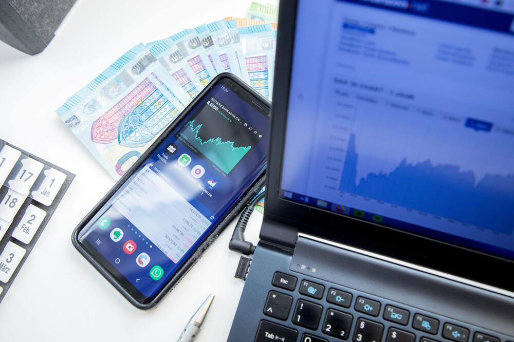 Smartphone, Laptop und Geldscheine auf einem Schreibtisch