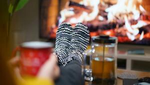 Gestrickte, schwarz-weiß gemusterte Haussocken an ausgestreckten Beinen vor einem flackernden ...