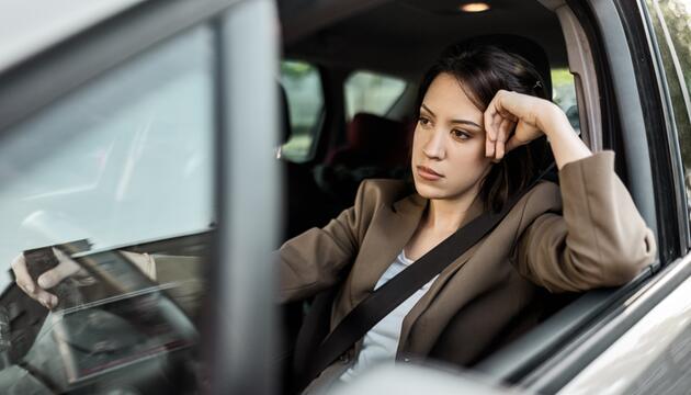 Genervte junge Frau sitzt in einem Auto.