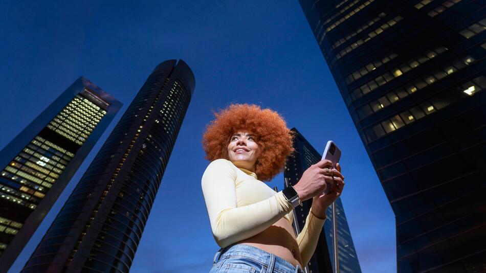 Eine Frau mit einem roten Afro steht vor Hochhäusern.