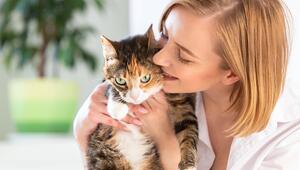 Lächelnde Frau in weißem Hemd küsst eine Katze.