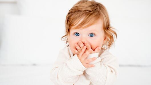 Rothaariges Kleinkind, das sich die Hände vor den Mund hält