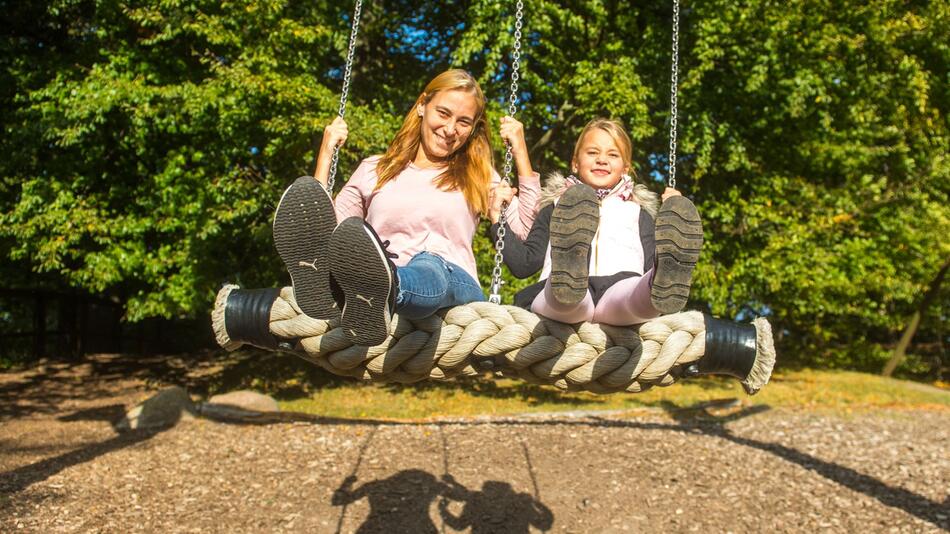 Frau schaukelt mit ihrer Tochter auf einem Spielplatz