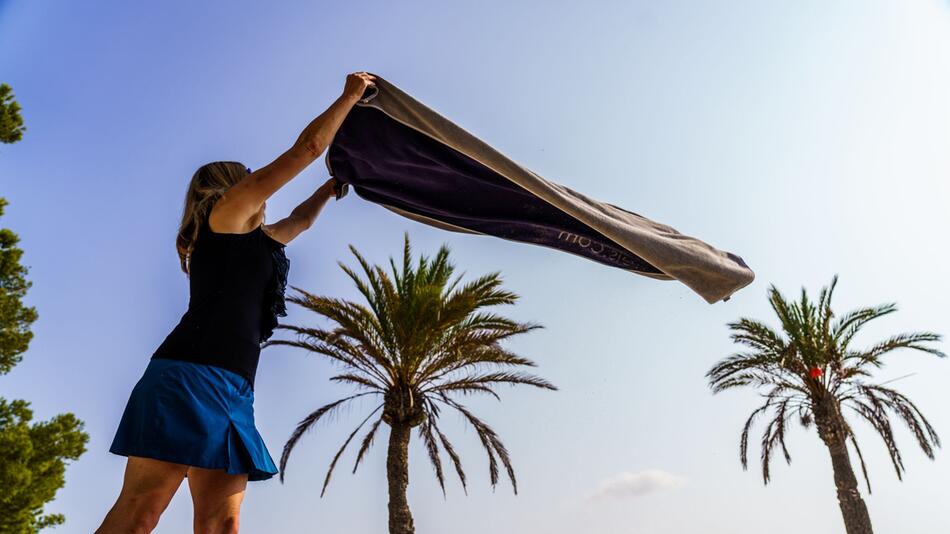 Eine Frau breitet am Strand ihr Handtuch aus