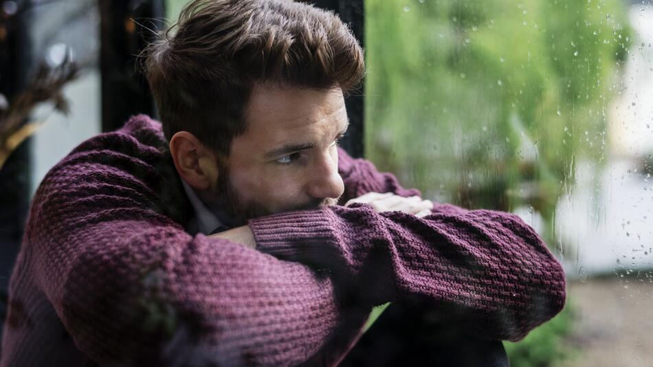 Mann schaut nachdenklich aus dem Fenster