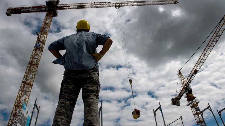 Mann blickt auf einer Baustelle auf zwei Kräne