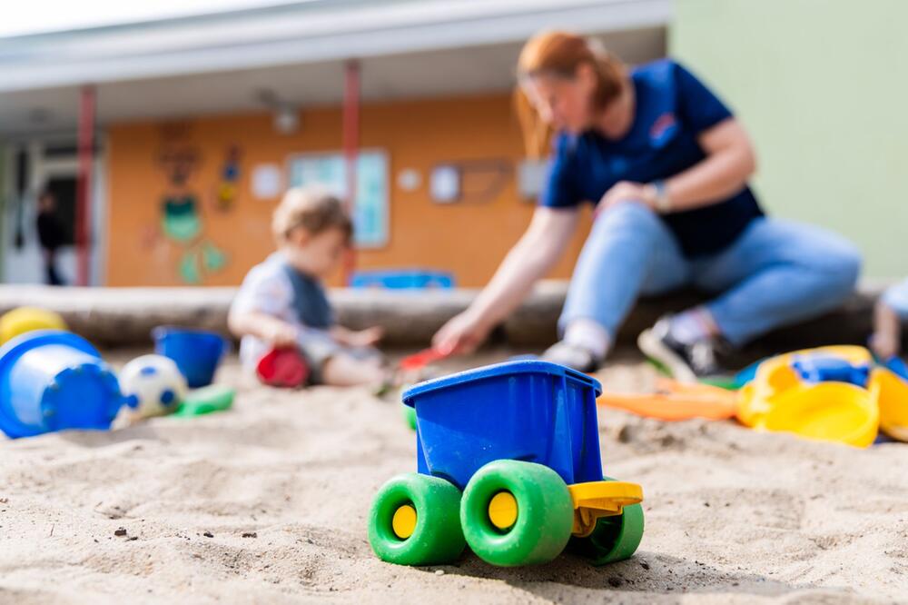 Ein Kind spielt mit einer Erzieherin im Sandkasten